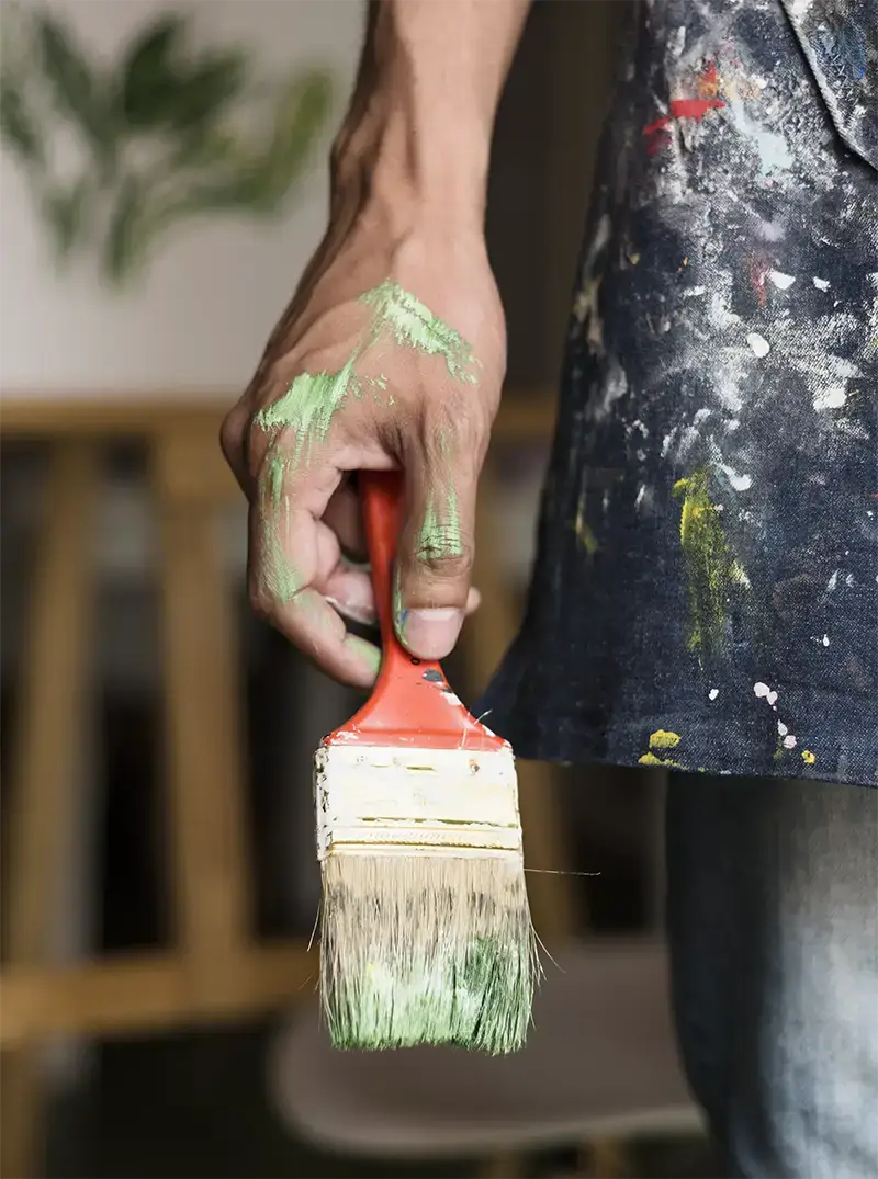 Pintor sosteniendo una brocha con la mano y el uniforme manchado de diferentes colores de pintura
